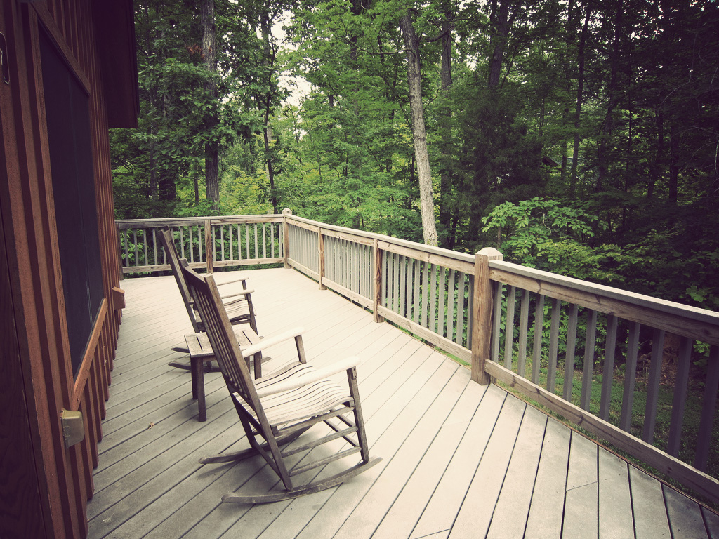 A scenic view from a cabin deck in the woods with a comfy rocking chair.